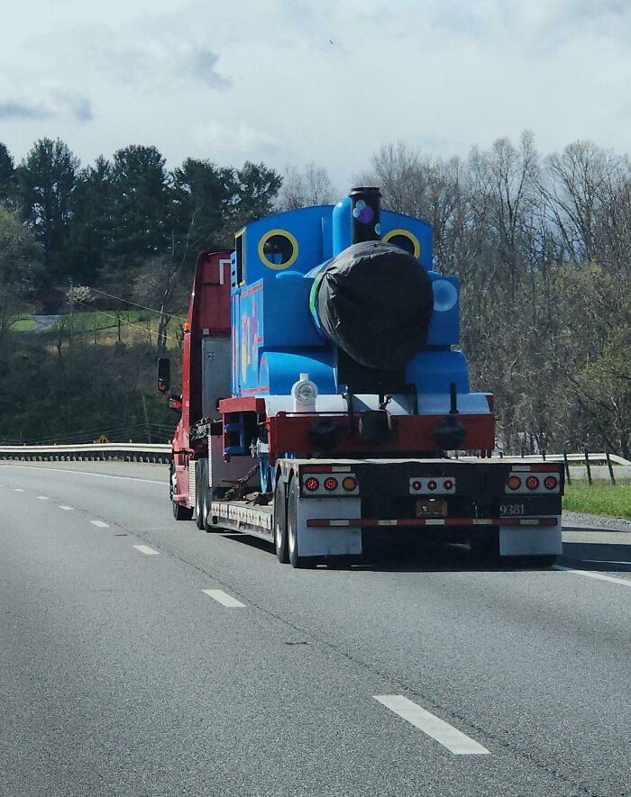 Blue train engine being transported on a truck down the highway, providing interesting things on the road.