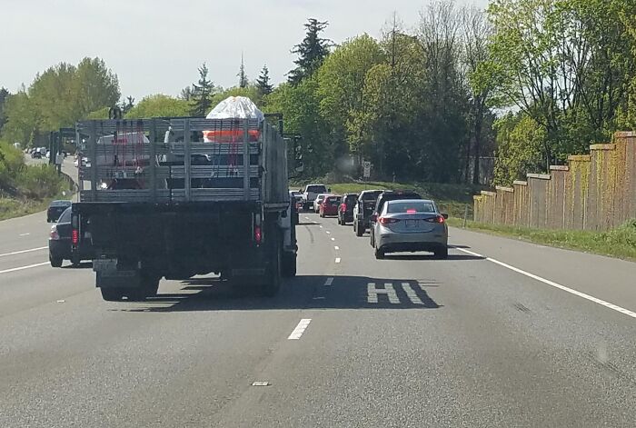 Truck carrying a wrapped item in traffic on a tree-lined road, showcasing interesting things on the road.