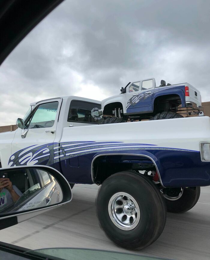 Unique truck on the road carrying a smaller replica in its bed, both featuring matching blue and white designs.