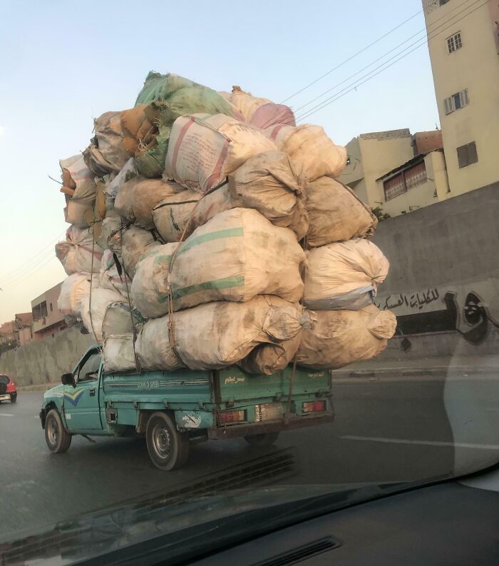 Overloaded truck carrying large bags down the road, showcasing interesting things on the road with urban buildings in background.