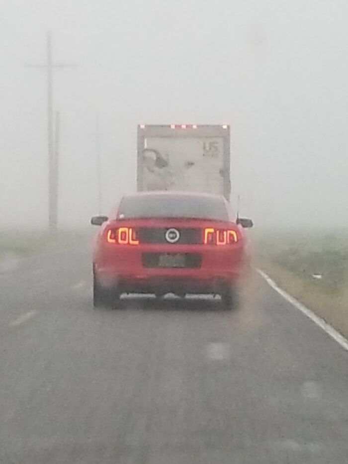 Red car on foggy road with playful taillights reading "LOL RUN," a quirky sight seen while driving.