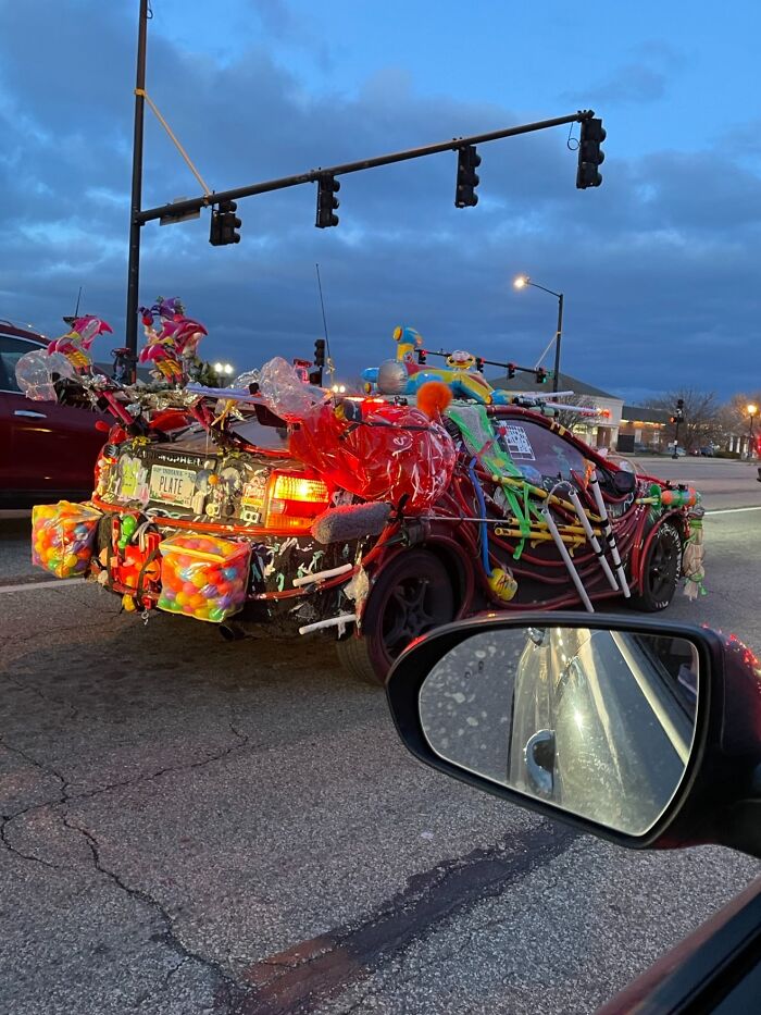 Decorated car adorned with colorful objects and toys on the road at dusk.