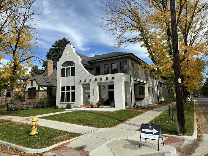 Modern white house on a corner lot with a unique facade, surrounded by fall foliage.