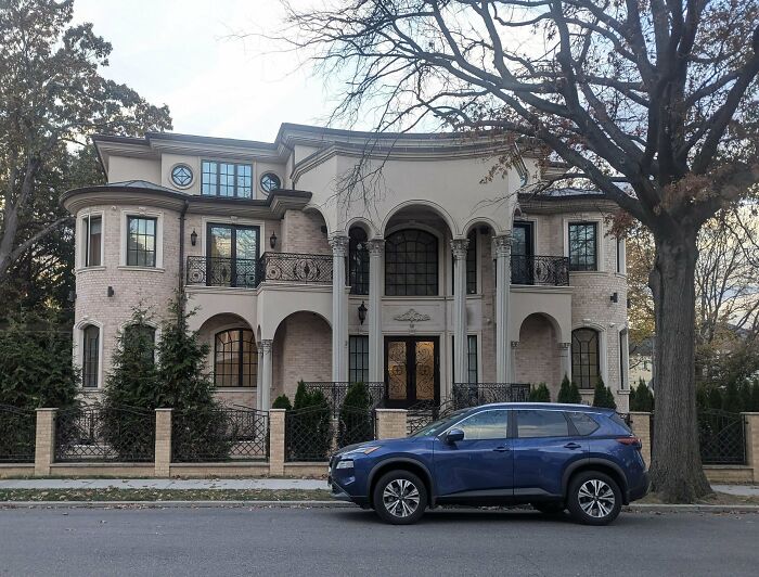 Luxurious mansion with ornate architecture and a blue SUV parked in front, highlighting that money can't buy taste in design.