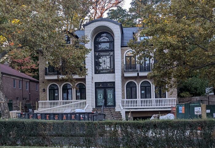 Luxurious mansion with ornate design and a large front entrance, surrounded by trees, demonstrating money can't buy taste.