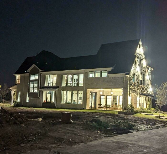 Luxury house at night, brightly lit with large windows, highlighting that money can't buy taste in home design.