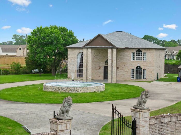 Luxurious house with pillars and circular driveway, showcasing that money can't buy taste, featuring lion statues and a fountain.