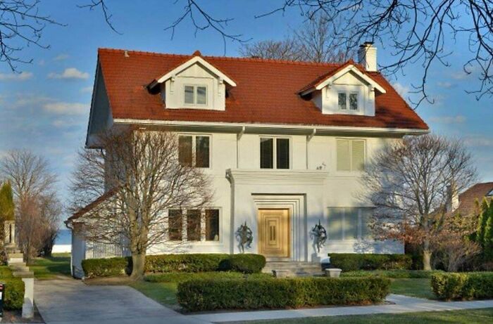 Large white house with red roof, surrounded by bare trees and a neat lawn, showcasing that money can't buy taste.