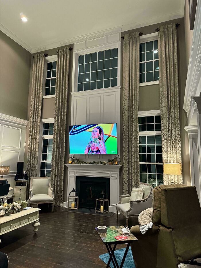 Luxurious living room with high curtains, ornate chairs, and large TV over fireplace, illustrating that money can't buy taste.