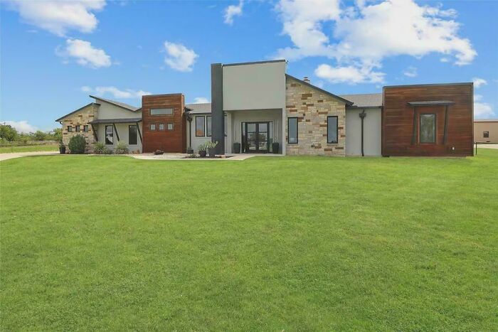 Modern house with mixed materials and asymmetrical design on a large green lawn, showcasing money can't buy taste.