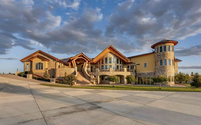 Luxurious mansion with grand staircase and stone facade under a cloudy sky, exemplifying how money can't buy taste.