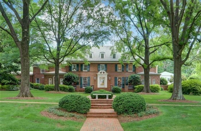 Grand brick mansion surrounded by lush trees, demonstrating that money can't buy you taste.