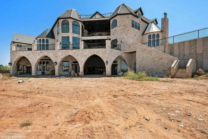 Luxurious yet tasteless mansion with mixed architecture, featuring large arches and an unfinished dirt landscape.