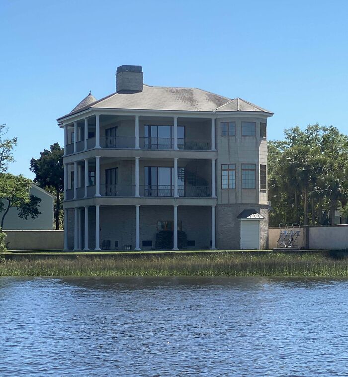 Unusual house design with mismatched architectural elements by a lake, reflecting that money can't buy taste.