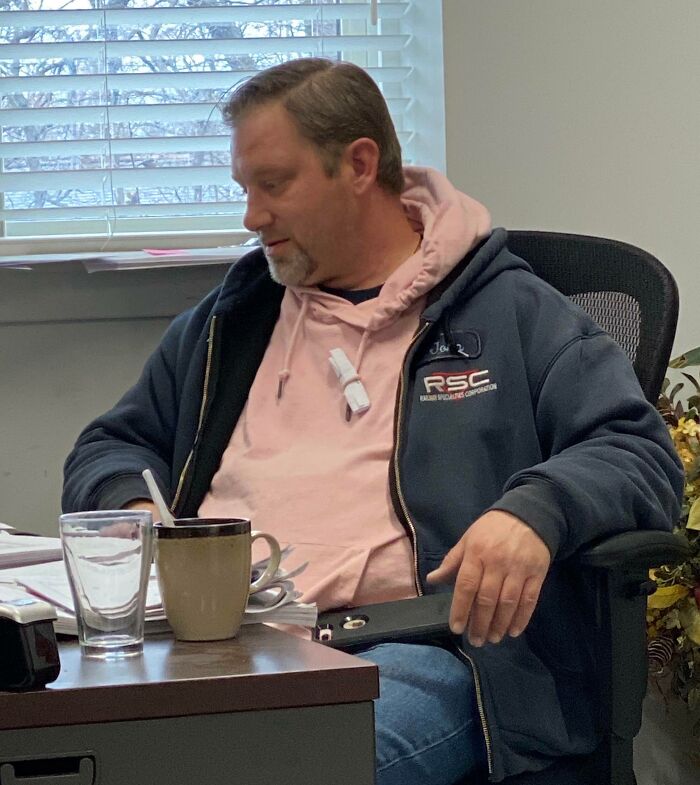 Man in casual attire with a hoodie and jacket, seated at a desk with a mug and papers, embodying Good-Funny-Bosses vibes.