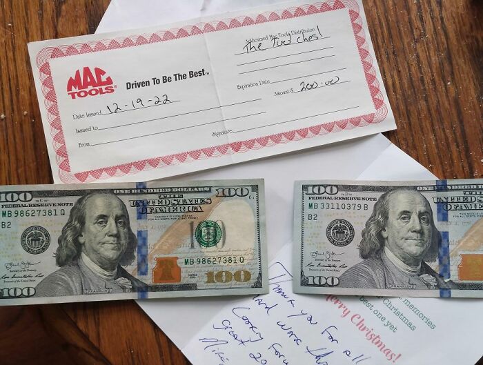 Two $100 bills, a Mac Tools check, and a thank you note from a funny boss on a wooden table.