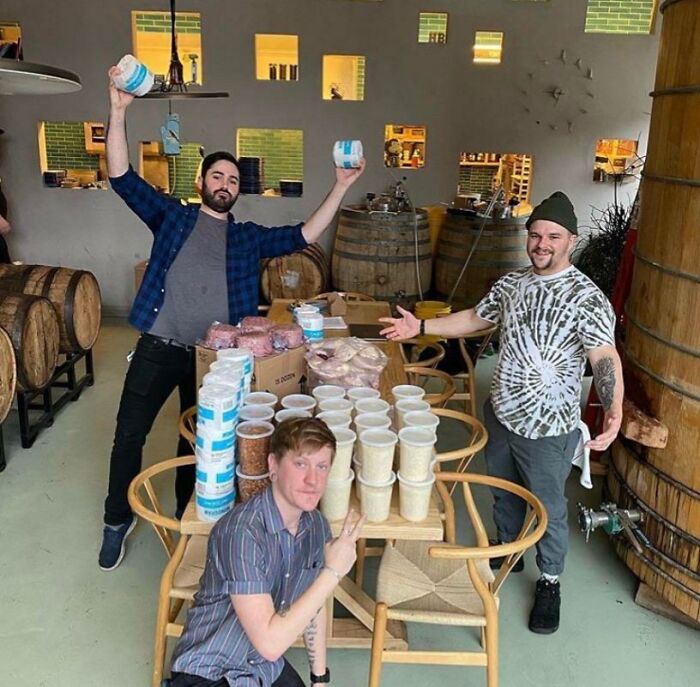 Three cheerful men in a cozy brewery setting, surrounded by stacks of food containers on a wooden table, showcasing good-funny-bosses.