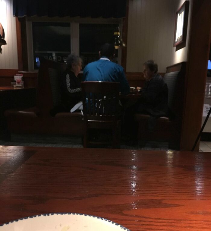 Three people at a restaurant booth having a conversation with a good-funny-boss in a blue shirt.