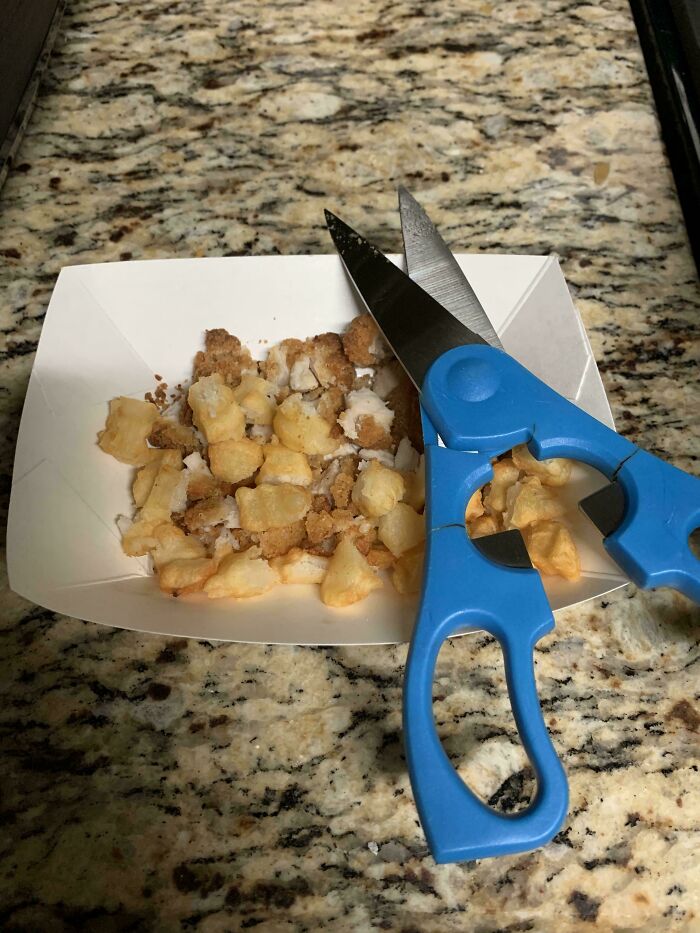 Scissors cutting chicken nuggets on a tray, showcasing a parenting genius trick.