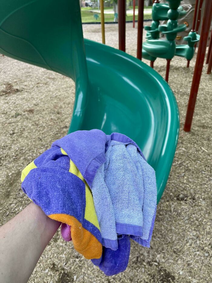 Hand holding colorful towels at playground slide, showcasing parenting genius tricks.