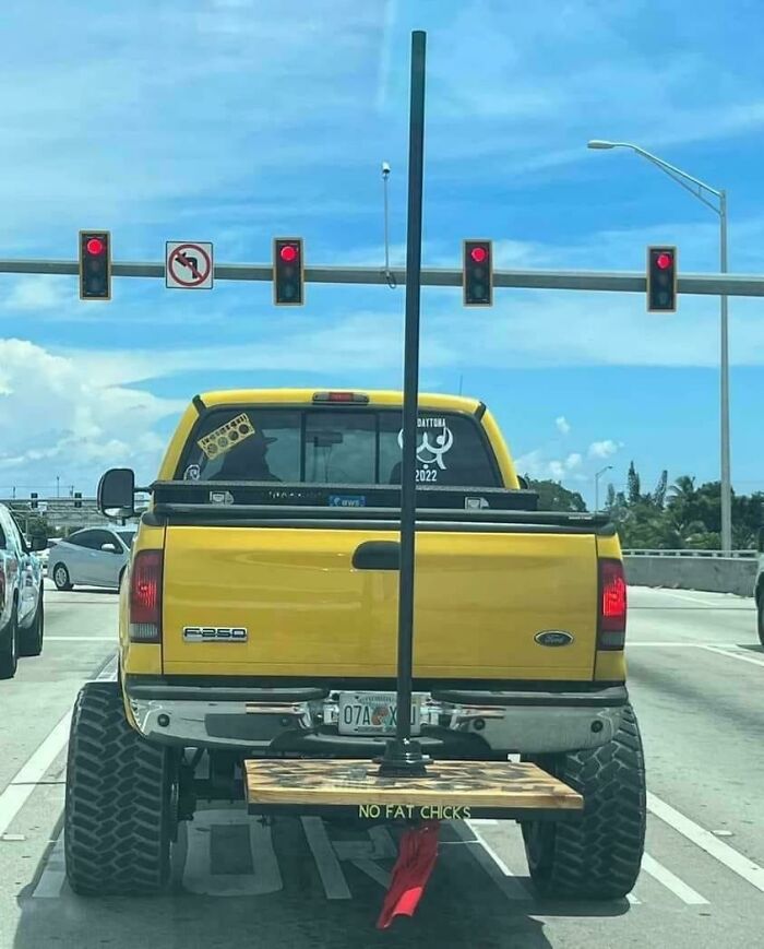 Yellow truck with a pole and sign on the back, illustrating car-fails at a traffic light.