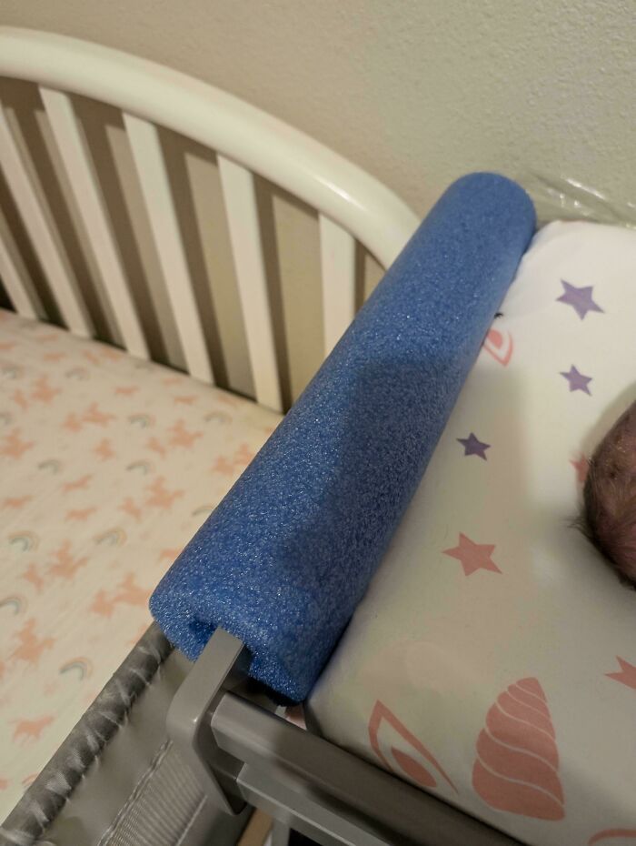 Blue pool noodle used as a bumper on a crib for child safety, showcasing a creative parenting trick.