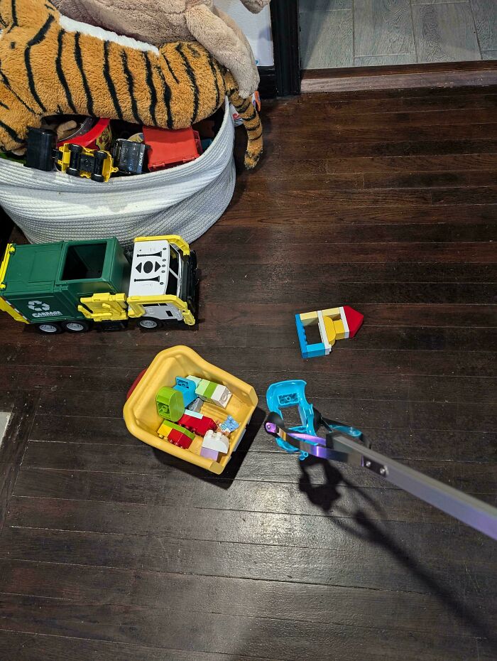 Toys on the floor being picked up with a grabber tool, demonstrating parenting genius tricks.