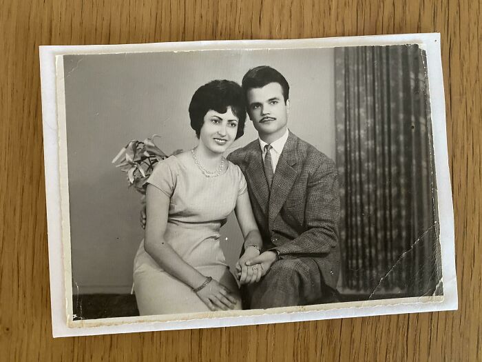 Vintage couple in 60s fashion, with woman in a classic dress and man in a suit, posing in a retro-styled setting.