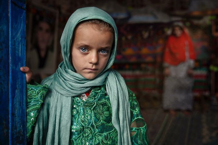 Young girl in a green dress and headscarf, standing thoughtfully, showcasing captivating photography by Hamed AlGhanboosi.