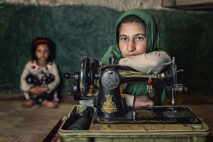 A woman in traditional attire with a sewing machine; captivating photograph by Hamed AlGhanboosi.