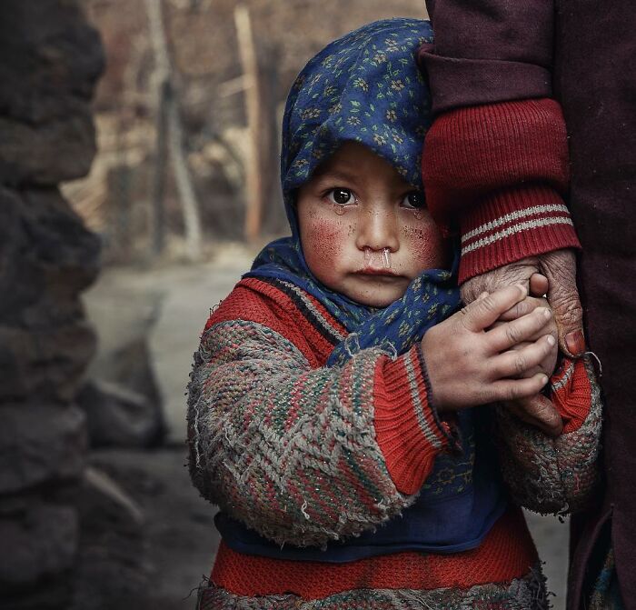 A child in a colorful sweater and headscarf holding an adult's hand, captured in a captivating photograph by Hamed AlGhanboosi.