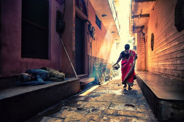 A person in a vibrant sari walks down a sunlit alley, capturing the essence of Hamed AlGhanboosi's captivating photographs.