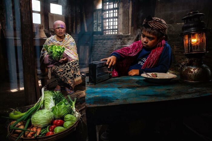 Interior scene by Hamed AlGhanboosi, featuring a boy with a radio and a woman holding fresh vegetables.