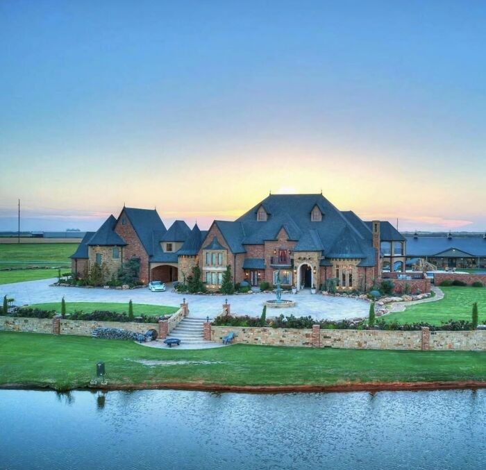 Luxurious mansion at sunset with a large front yard and lake, showcasing that money can’t buy taste.