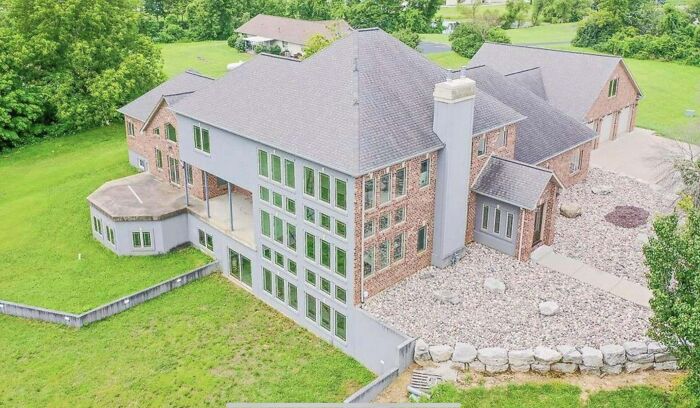 Large brick house with unusual window placement, surrounded by green grass, illustrating that money can't buy taste.