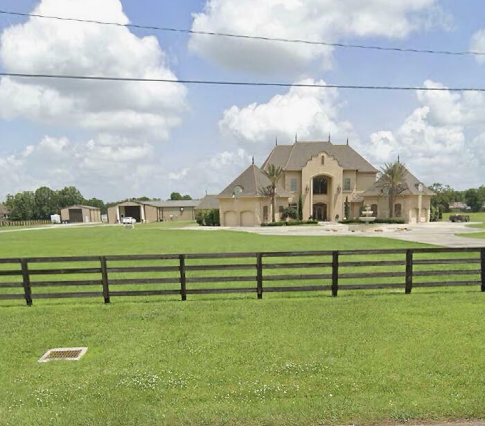 Luxurious house with large yard and fence under cloudy sky, showcasing that money can't always buy taste.