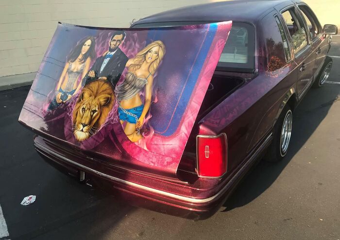 Car-fails: Customized car with painted trunk featuring lion and figures, parked in a lot.