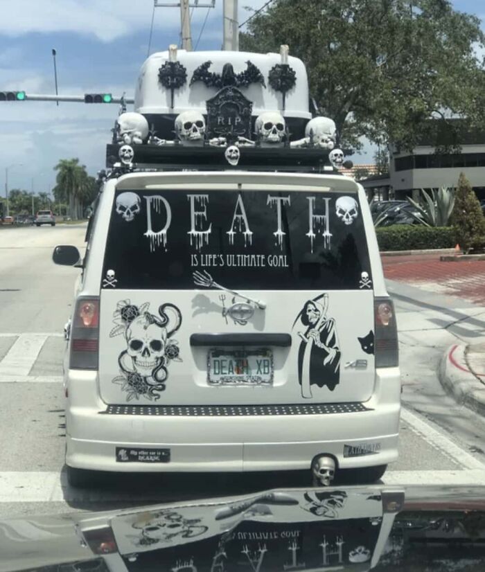 A car with skulls, grim reaper decals, and "DEATH" text, exemplifying a spooky-themed car-fail on a street.