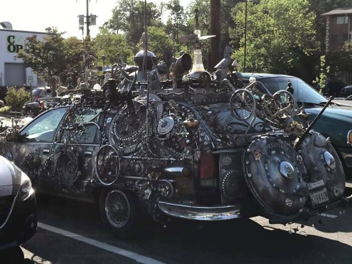 Car covered in decorative objects, showcasing extreme customization and creative car-fails in a parking lot.