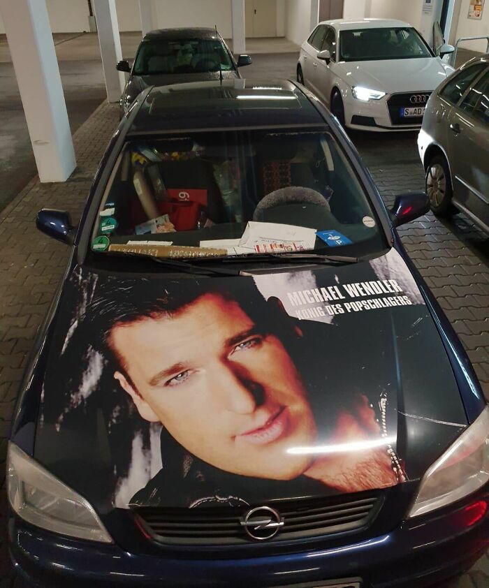 Car-fails: A car with a large celebrity face decal on the hood, parked in a garage.