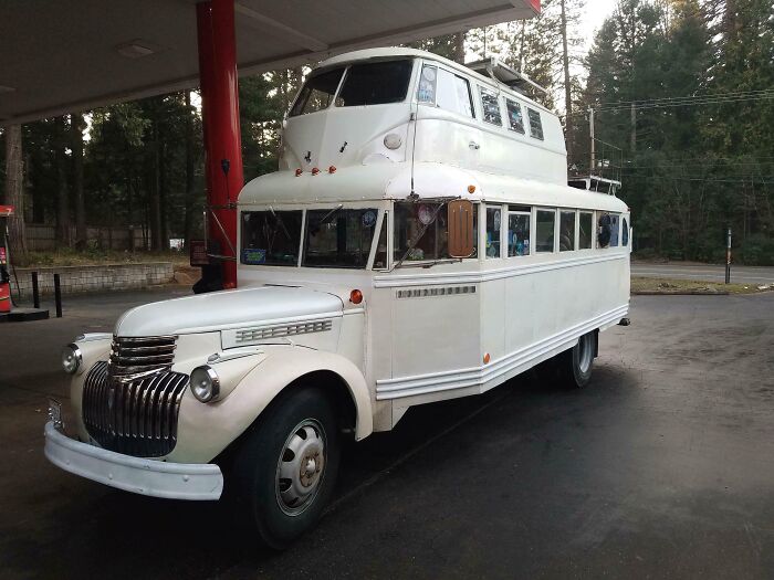 Unusual car-fails design with a bus carrying a boat on top at a gas station.