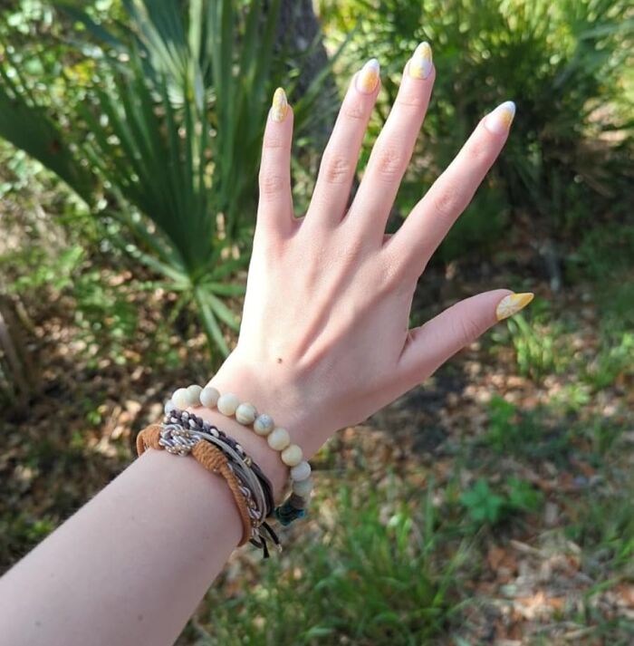 Woman's hand with unique bracelets, yellow nails, outdoors.