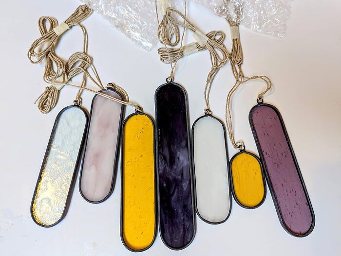 Colorful stained glass suncatchers, unique gifts for women, lay on a table with twine strings attached.