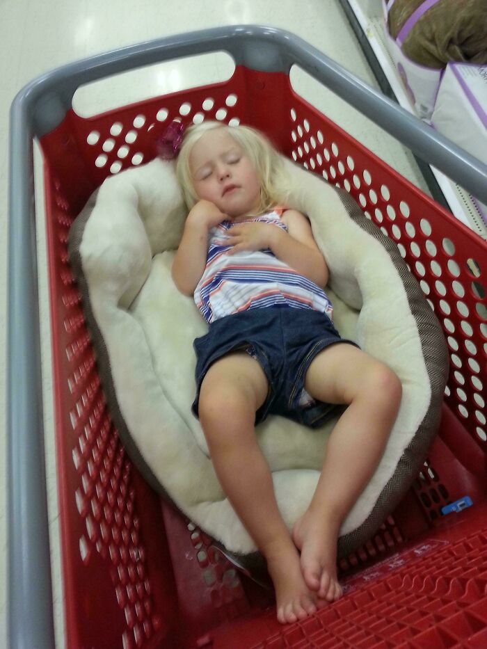 Child sleeping comfortably in a shopping cart, showcasing parenting genius tricks.