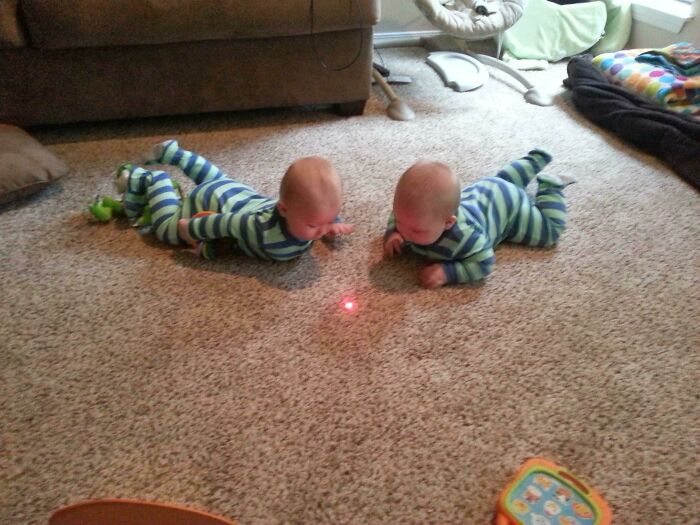 Twins in striped pajamas lie on a carpet, captivated by a red dot, illustrating parenting genius tricks.