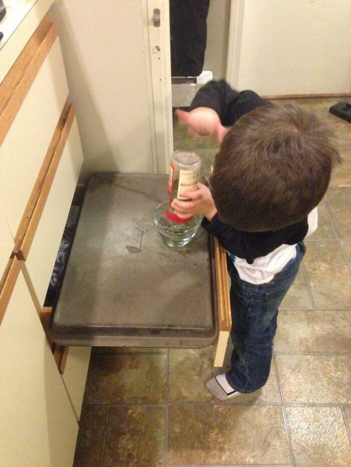 Child using an open oven door as a table in the kitchen for a clever parenting trick.