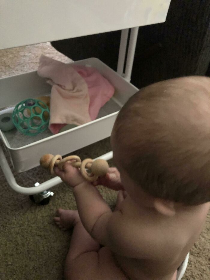 Baby playing with a wooden toy near a shelf, showcasing parenting genius tricks.