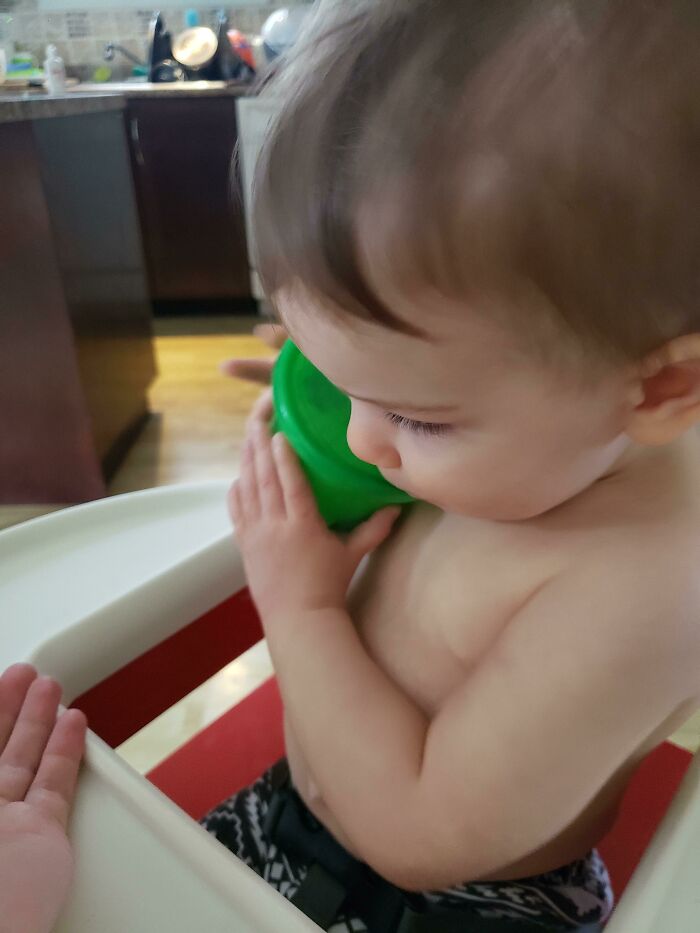 Toddler in a high chair holding a green cup, showcasing parenting genius tricks.