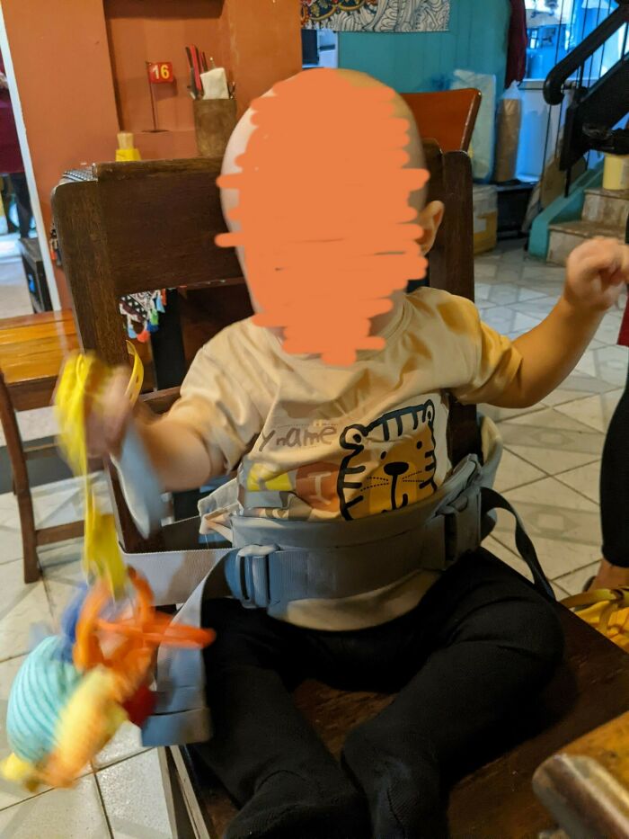 Baby safely secured in a high chair with a toy, showcasing parenting tricks.