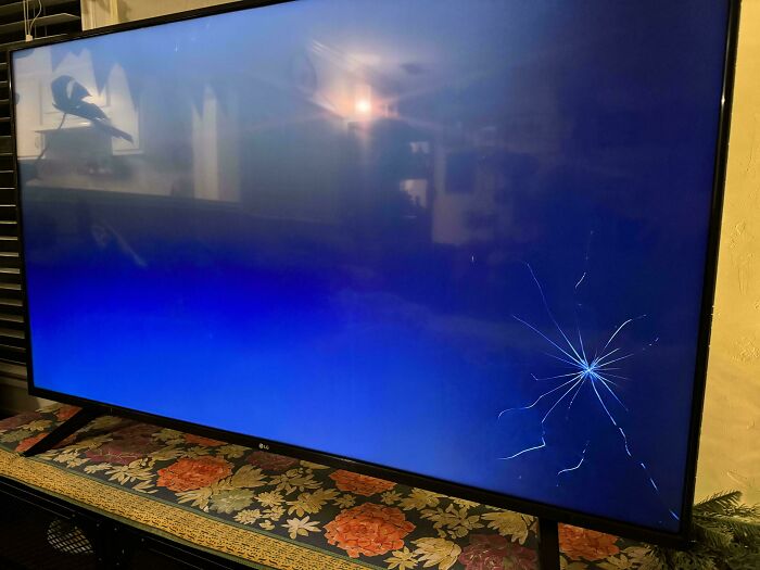 A cracked TV screen highlighting a Christmas accident in a dimly lit room.